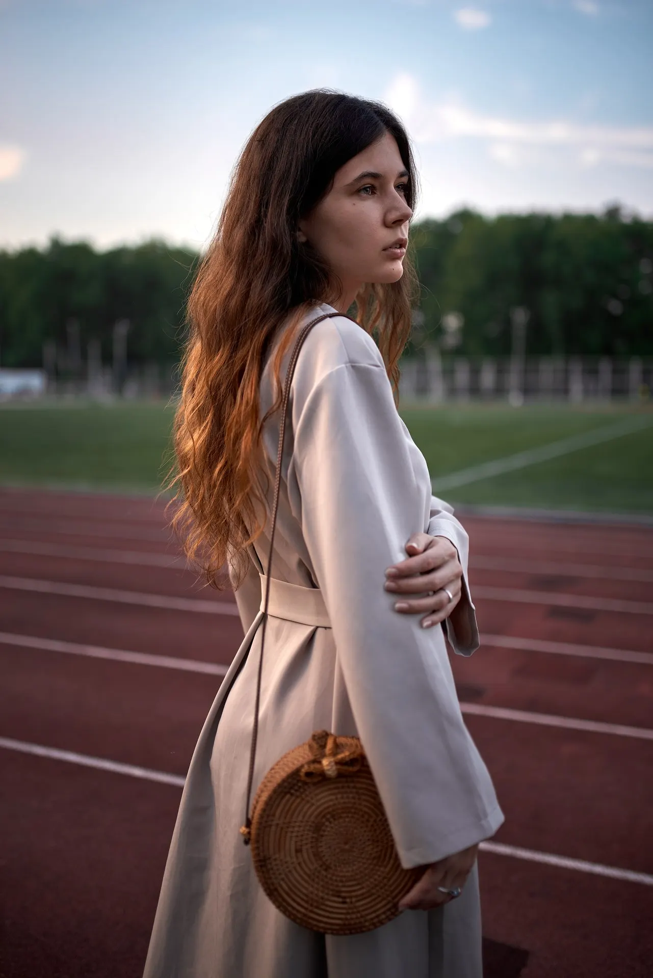 Nana in a long coat standing by an outdoor sports court