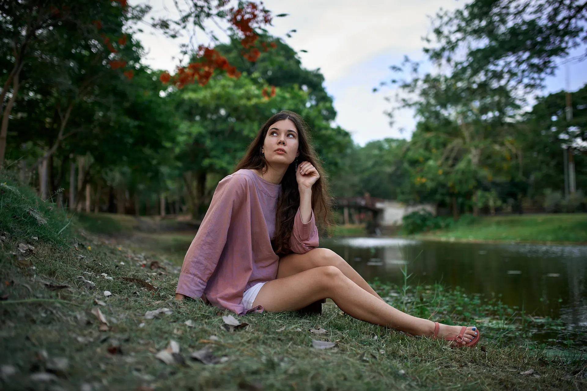 Nana seated by a lake in a pale pink shirt