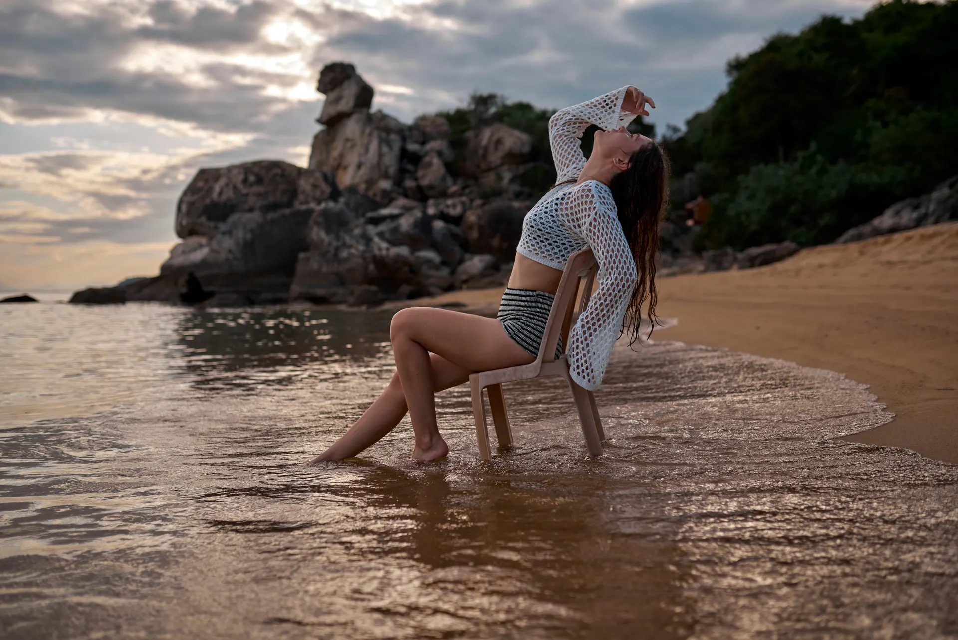Nana seated on a chair in the shallows beside coastal rocks