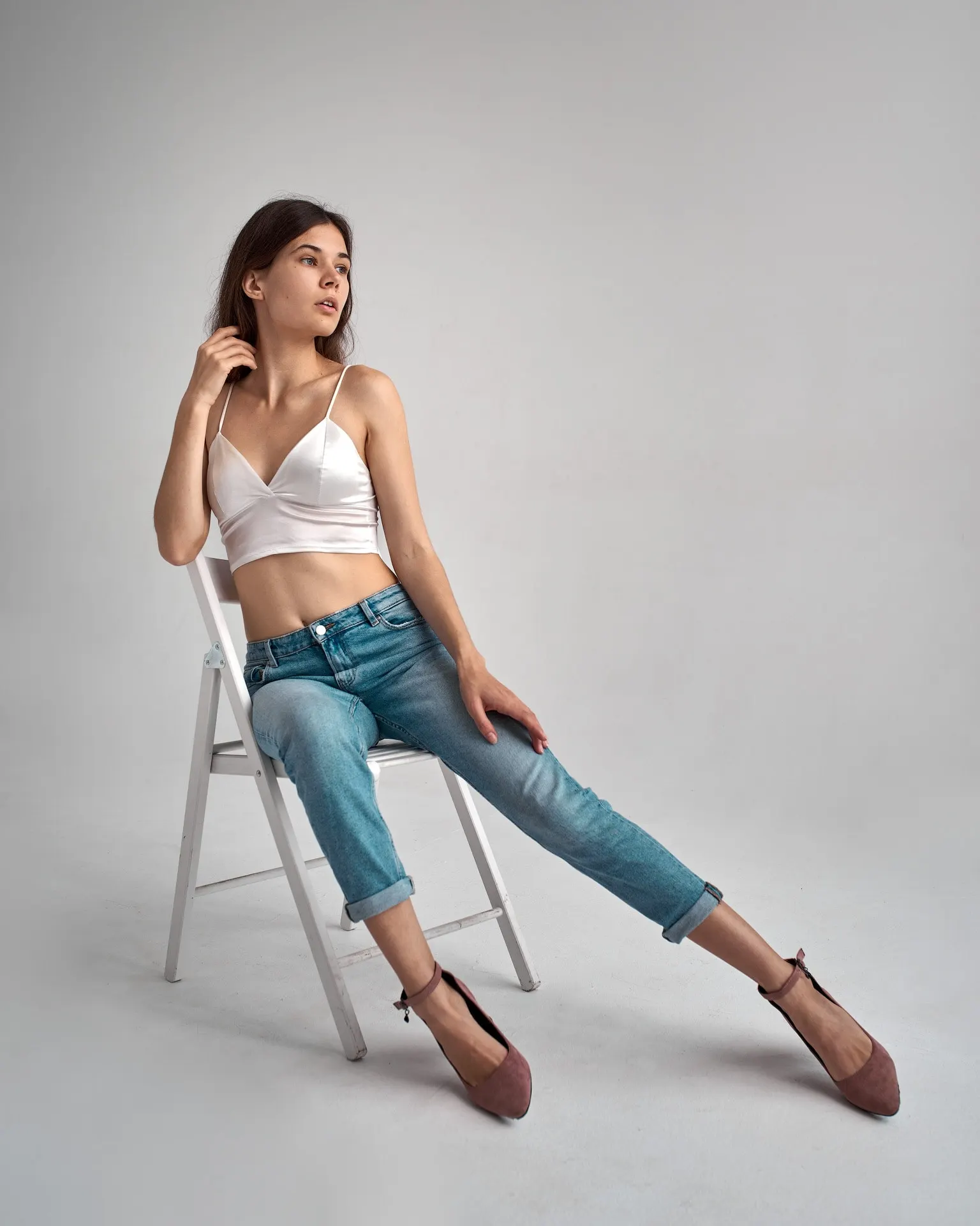 Nana in jeans and a white top seated on a studio chair