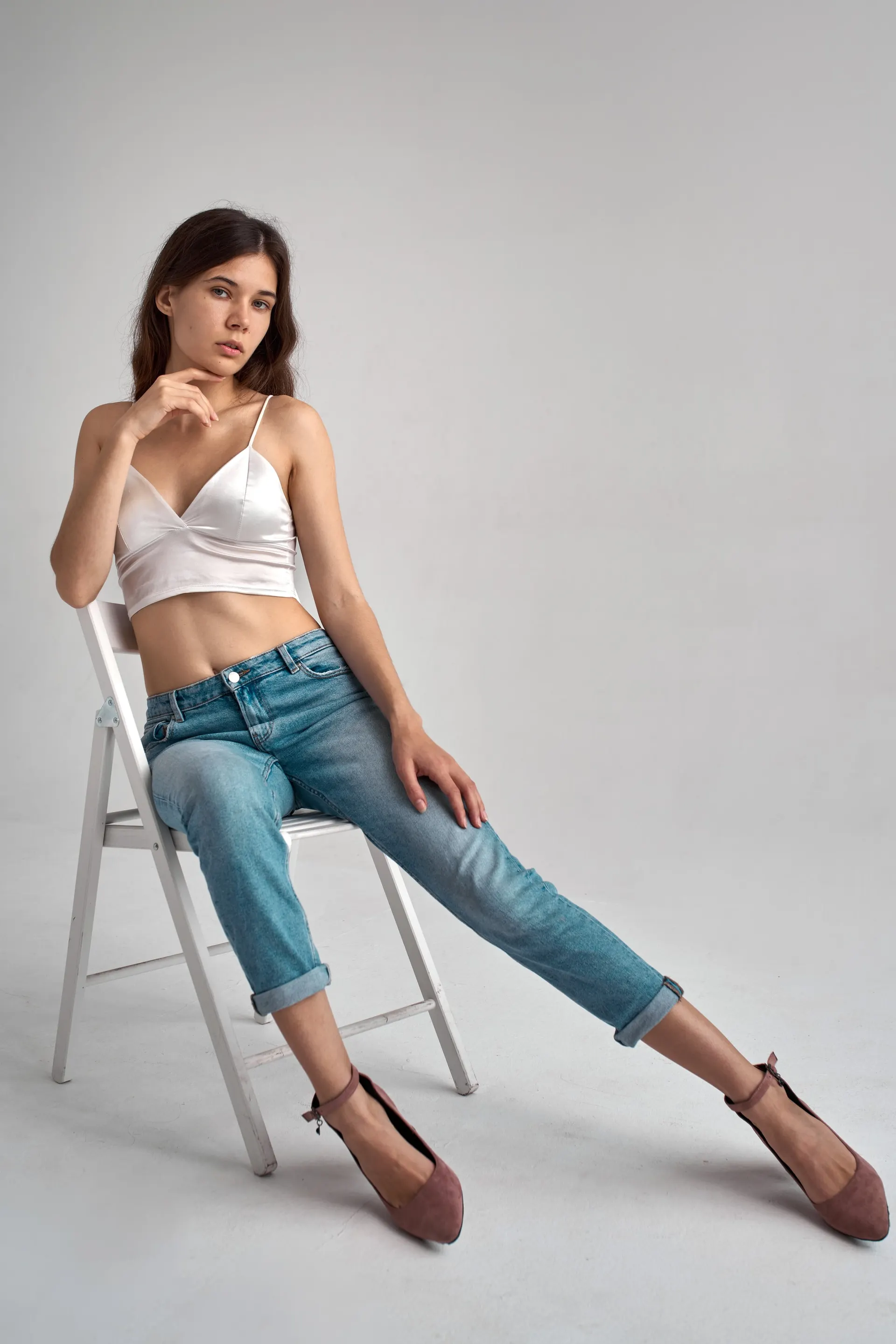 Nana seated on a white chair in jeans and heels
