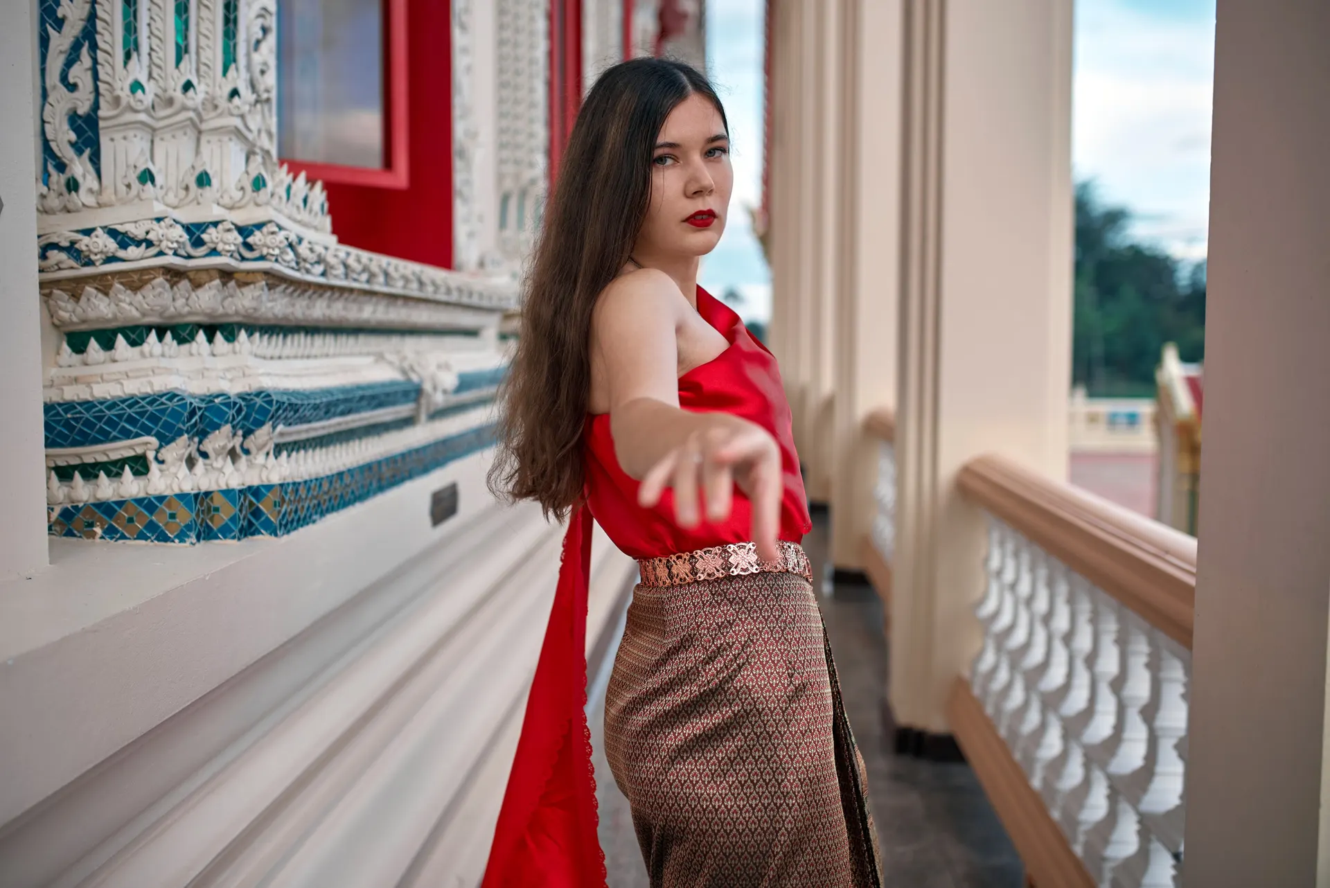 Nana in traditional Thai dress reaching toward the camera in a temple gallery