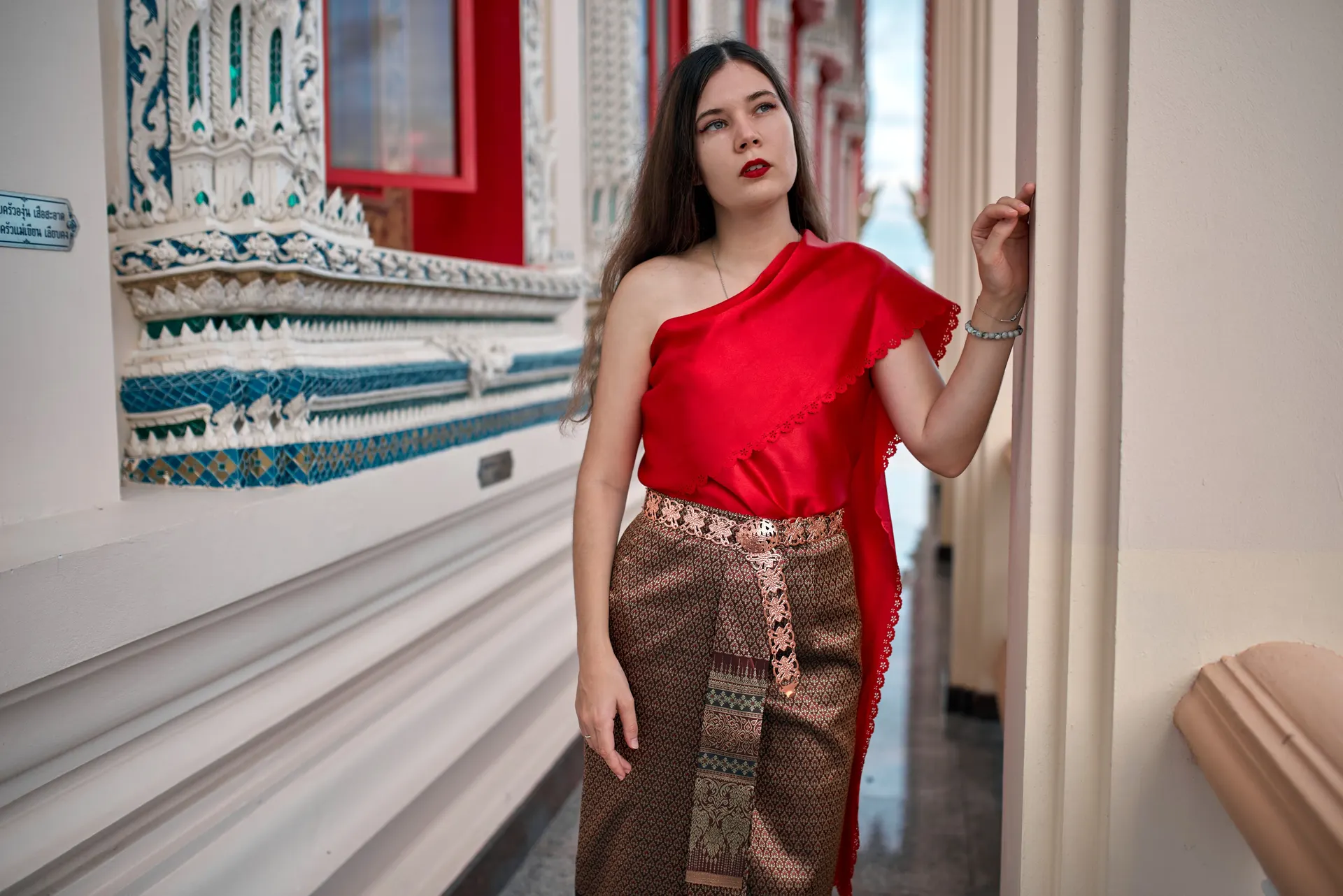 Nana in a red Thai shoulder sash and patterned silk skirt in a temple gallery