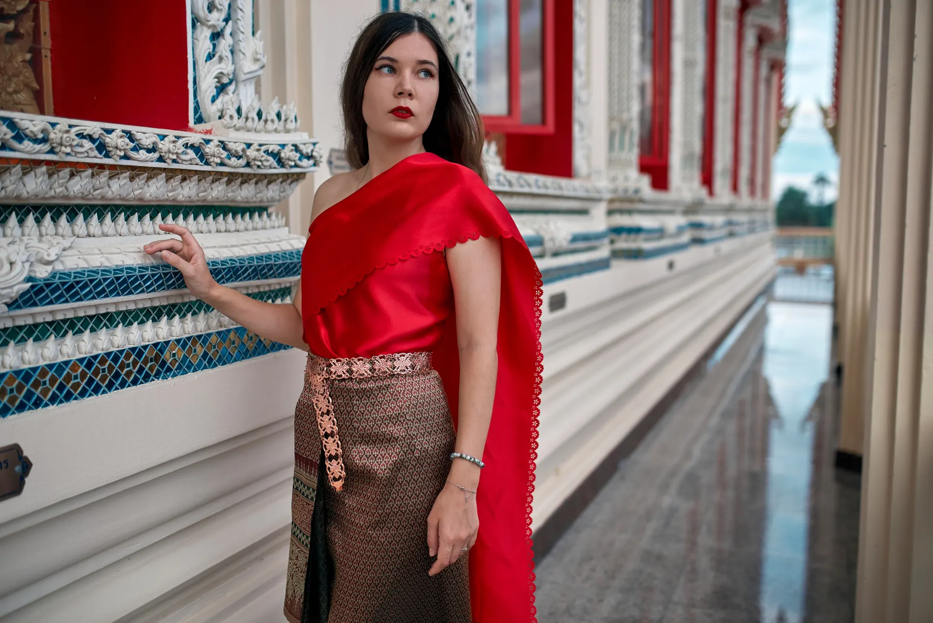 Nana in traditional Thai dress touching a carved temple wall