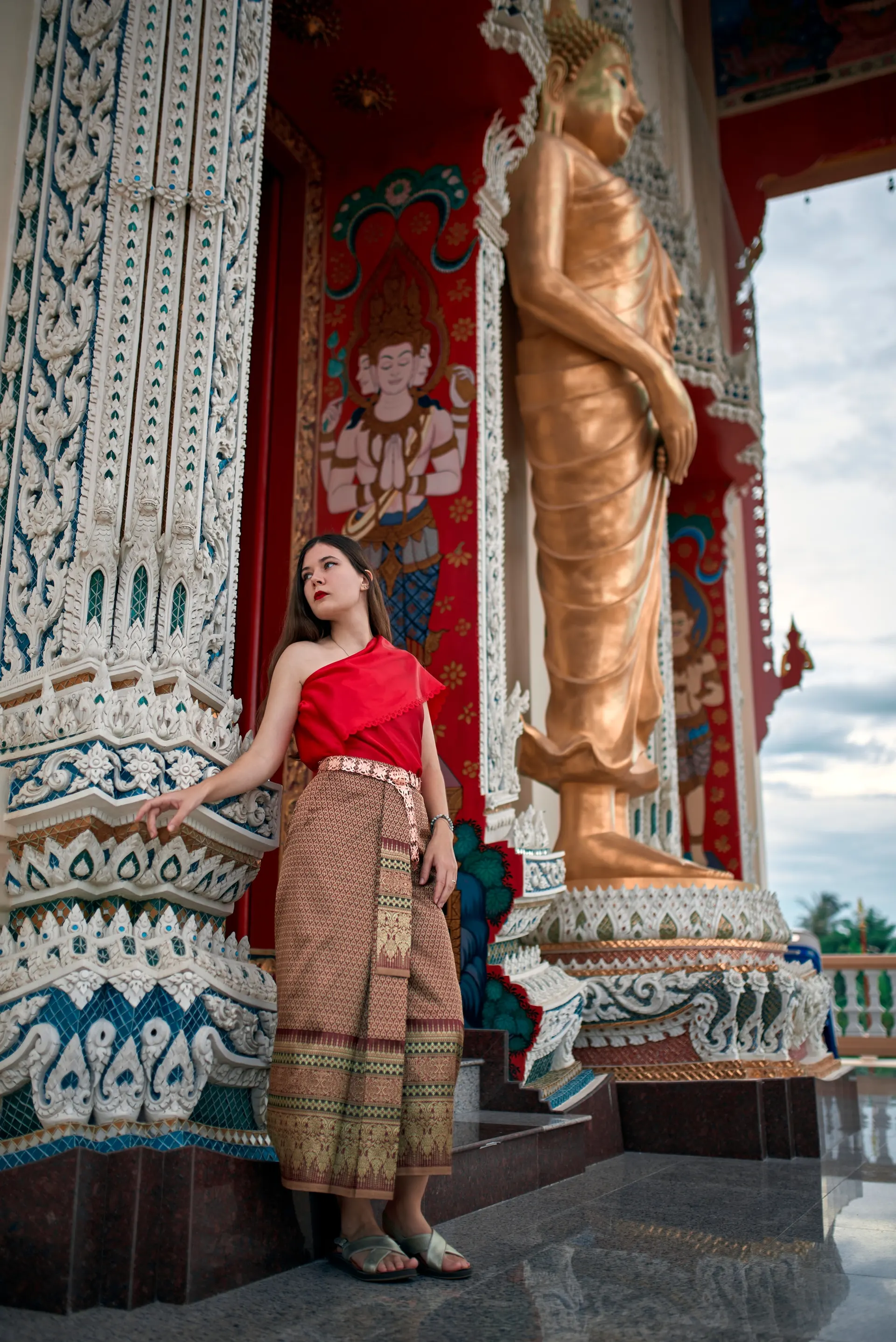 Nana in traditional Thai dress beside a golden standing Buddha at a temple entrance