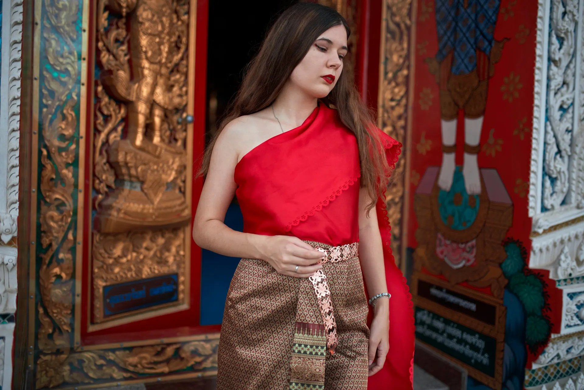 Nana in a red one-shoulder Thai top in front of a carved temple door