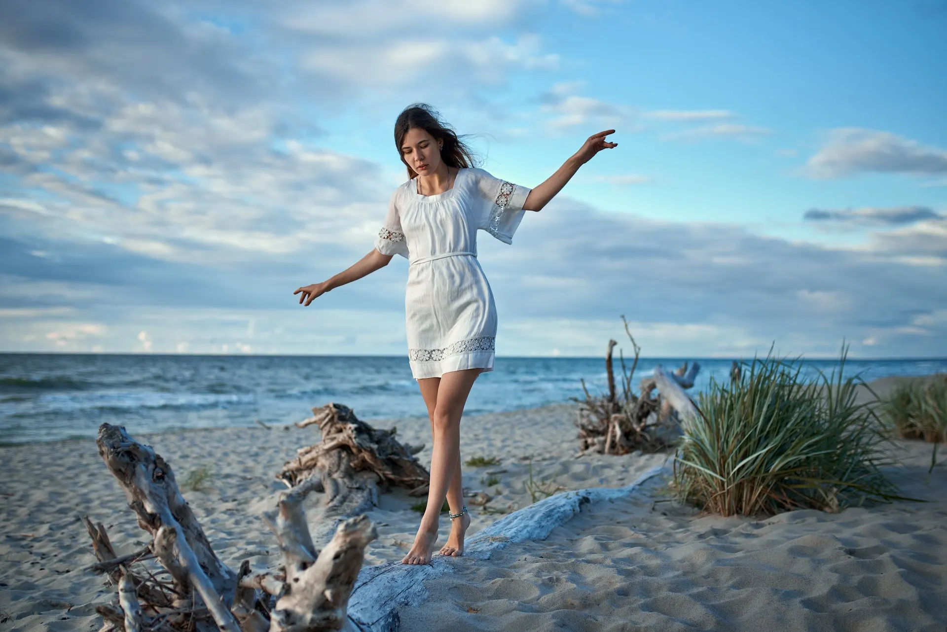 Nana in white standing on driftwood by the sea